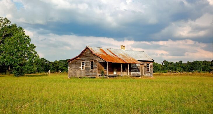 Abandoned house in middle of grassy field. 
